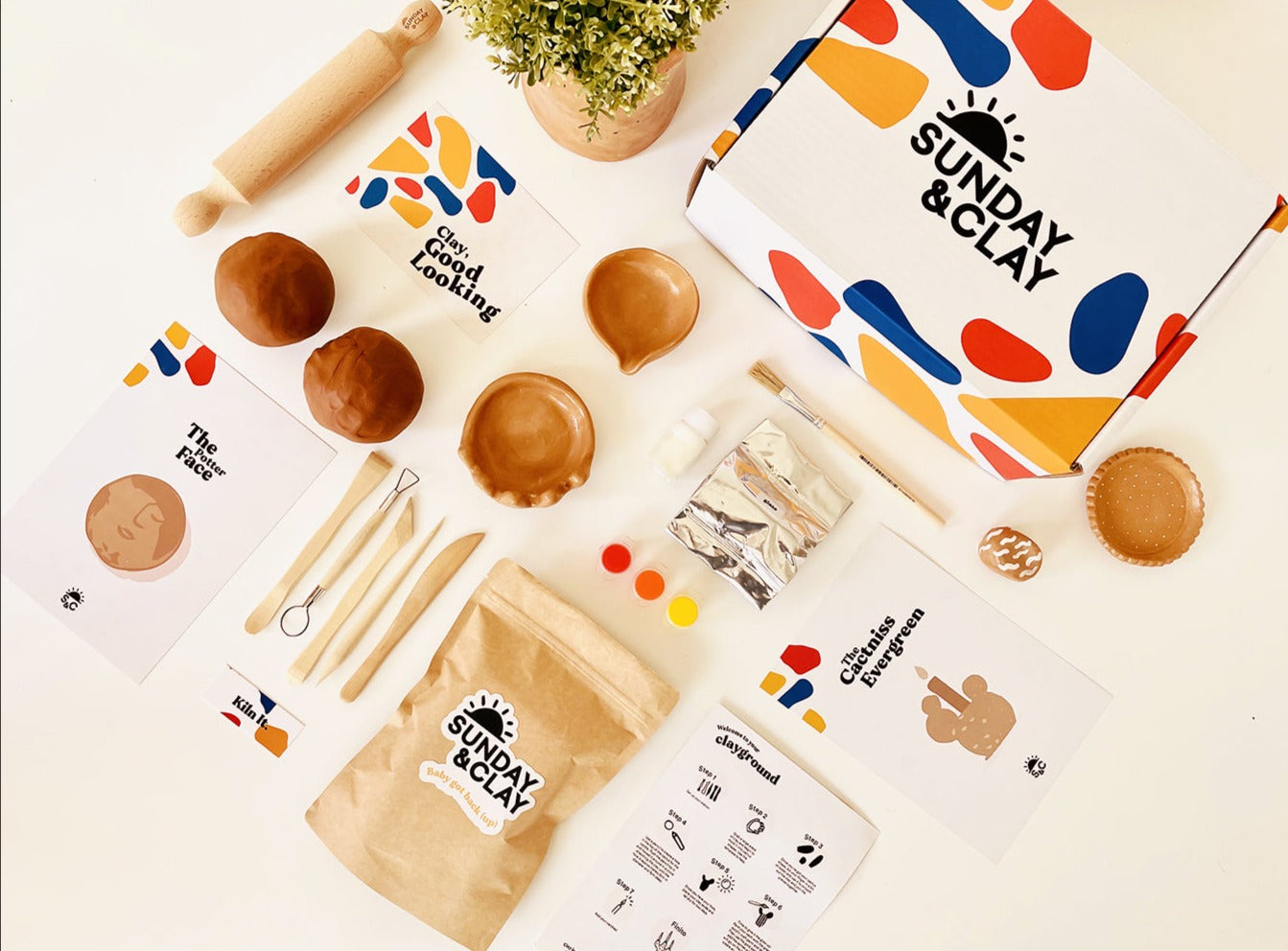 Clay, tools, instructions and paints included in the Clay kit laid out on a table in an interesting flat lay design