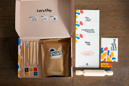 An open box on a wooden table showing all the pieces and tools included in the Air Dry Clay Kit